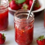 Homemade frozen strawberry jam in mason jars with fresh strawberries on a marble countertop; a vibrant, sweet preserve made using frozen strawberries.