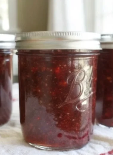 Homemade strawberry jam in glass canning jars with fresh strawberries and sugar on rustic wooden background
