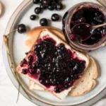 Homemade cherry jam recipe in glass jars with fresh cherries and wooden spoon on rustic kitchen counter