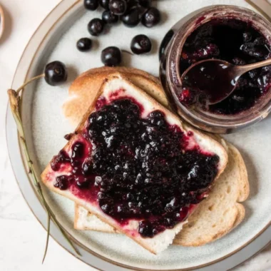 Homemade cherry jam recipe in glass jars with fresh cherries and wooden spoon on rustic kitchen counter