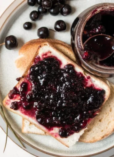 Homemade cherry jam recipe in glass jars with fresh cherries and wooden spoon on rustic kitchen counter