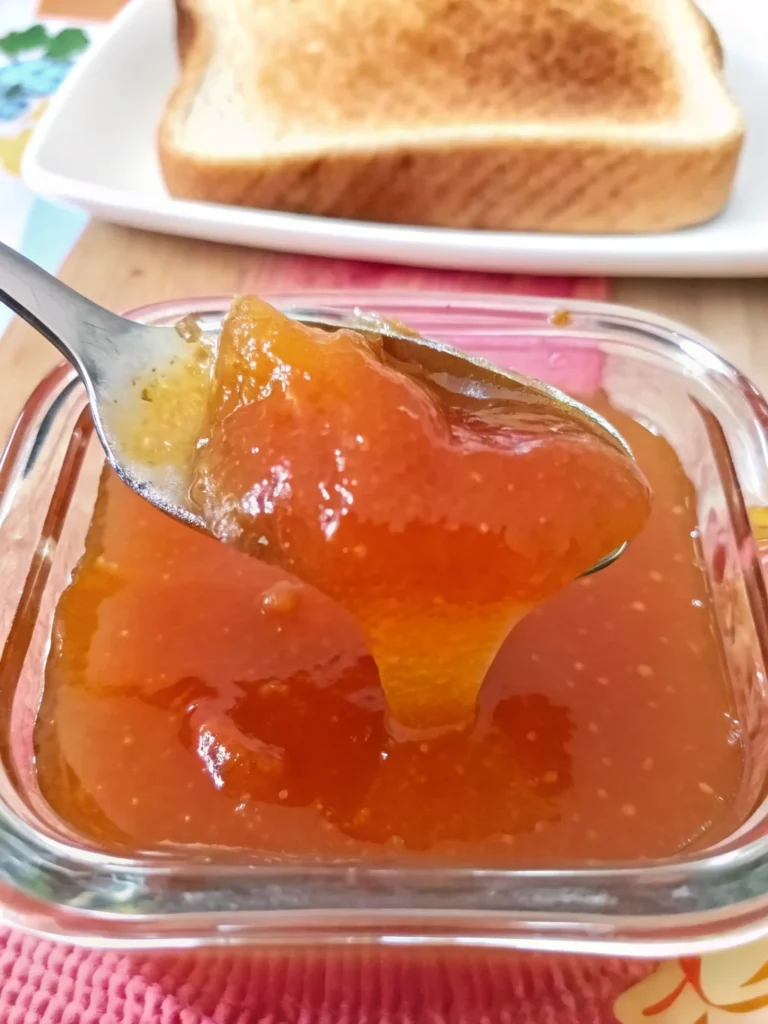 Homemade guava jelly jam in glass jar with fresh pink guavas and spreading knife on wooden cutting board