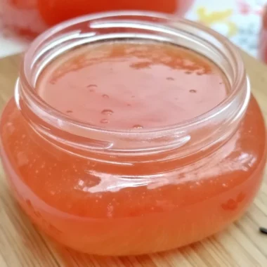 Homemade guava jelly jam in glass jar with fresh pink guavas and spreading knife on wooden cutting board