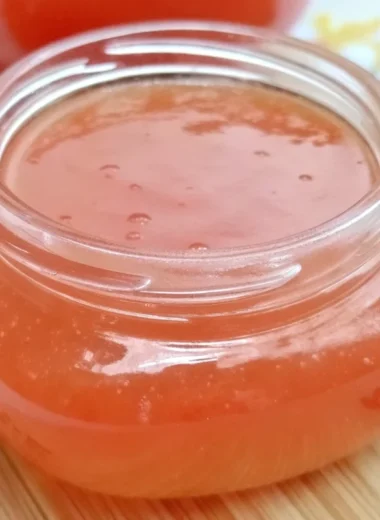 Homemade guava jelly jam in glass jar with fresh pink guavas and spreading knife on wooden cutting board