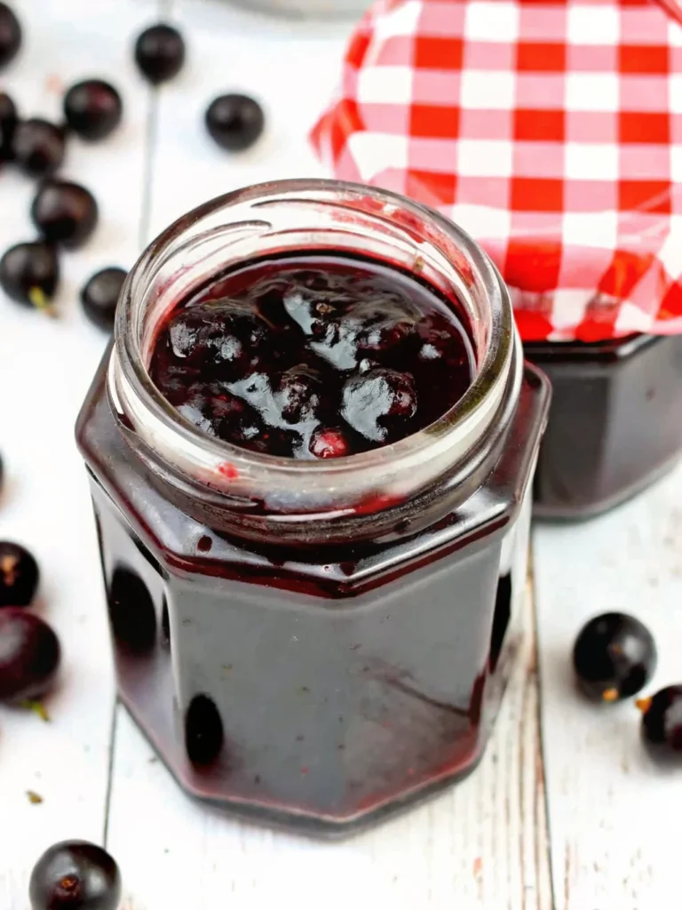 Homemade black currant jam recipe in glass jar with fresh black currants and ingredients on wooden table