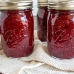 Easy homemade strawberry jam canning recipe showing fresh crushed strawberries, sugar, and pectin ingredients with mason jars and canning supplies for beginners
