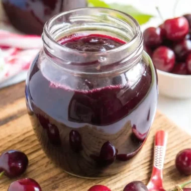 Homemade cherry jam recipe in glass jar with fresh cherries and spoon on wooden table