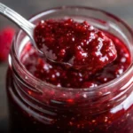 Homemade christmas jam recipes in glass jars with cranberries and strawberries on rustic wooden table with holiday spices