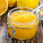 Golden Italian lemon jam in mason jars with fresh lemons and christmas jam recipe ingredients on rustic wooden table