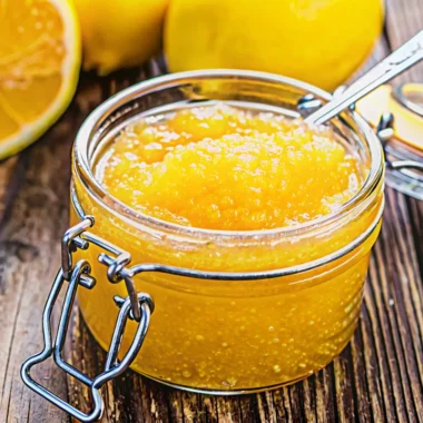 Golden Italian lemon jam in mason jars with fresh lemons and christmas jam recipe ingredients on rustic wooden table