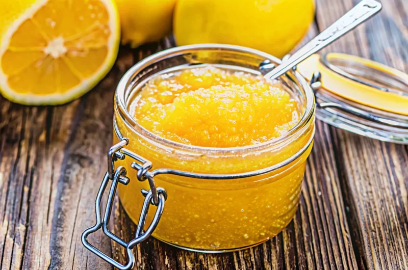 Golden Italian lemon jam in mason jars with fresh lemons and christmas jam recipe ingredients on rustic wooden table