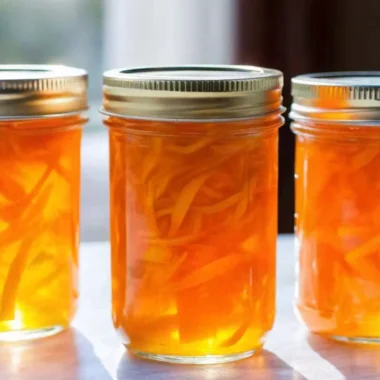 Homemade orange jam recipe with honey in glass jars showing golden citrus preserve with visible orange peel pieces, natural honey sweetening, healthy breakfast spread
