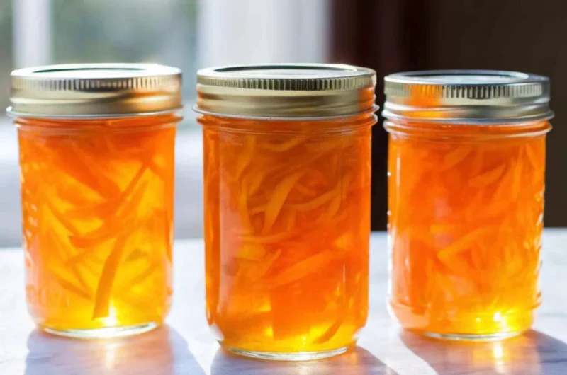 Homemade orange jam recipe with honey in glass jars showing golden citrus preserve with visible orange peel pieces, natural honey sweetening, healthy breakfast spread