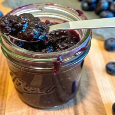 Homemade blueberry jam recipe without pectin in glass jar with fresh blueberries and wooden spoon