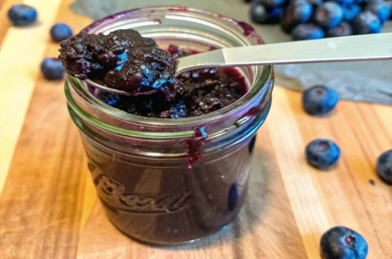 Homemade blueberry jam recipe without pectin in glass jar with fresh blueberries and wooden spoon