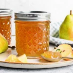 Homemade pear jam in glass jar with fresh pears and wooden spoon on rustic kitchen counter