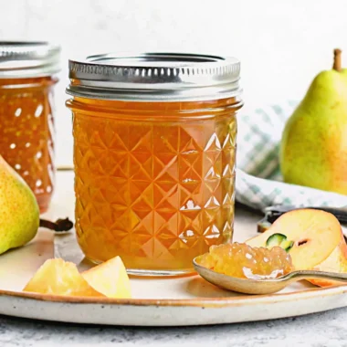 Homemade pear jam in glass jar with fresh pears and wooden spoon on rustic kitchen counter