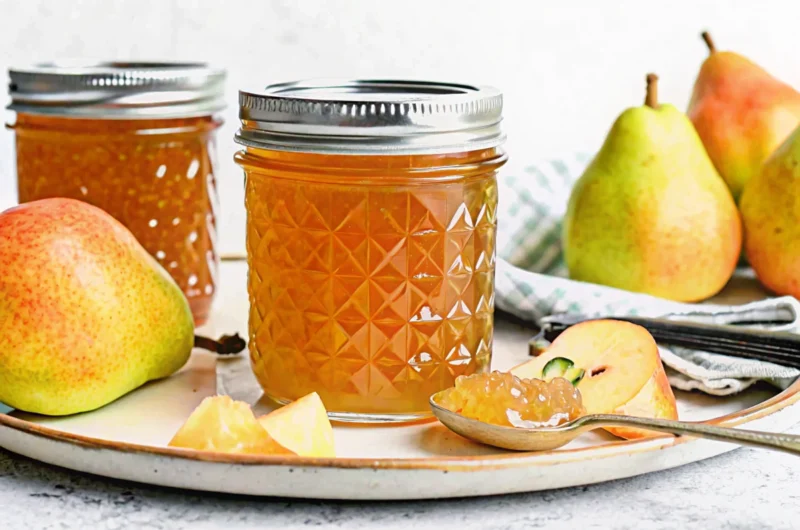 Homemade pear jam in glass jar with fresh pears and wooden spoon on rustic kitchen counter