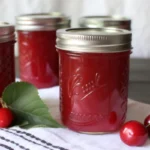 Homemade cherry jelly recipe ingredients including fresh tart cherries, sugar, and pectin arranged on kitchen counter with canning supplies