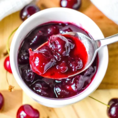 Homemade cherry jelly recipe no pectin in glass jar with fresh cherries scattered around wooden cutting board