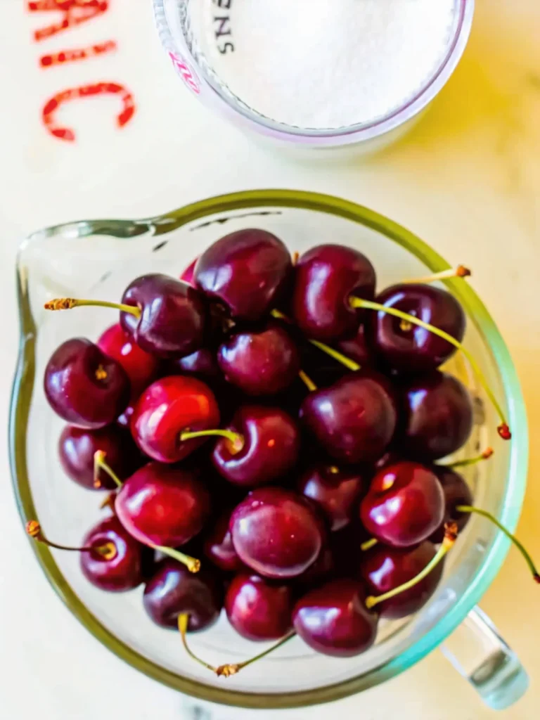 Homemade cherry jelly recipe no pectin in glass jar with fresh cherries scattered around wooden cutting board