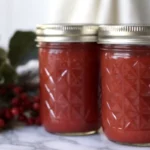 Homemade autumn olive jam in glass mason jars with fresh autumn olive berries scattered around on rustic wooden table