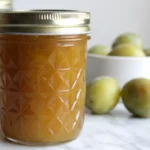 "Homemade greengage jam recipe in sterilized glass jars with fresh greengage plums and lemon on wooden cutting board
