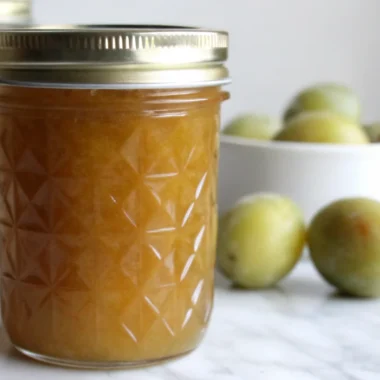 "Homemade greengage jam recipe in sterilized glass jars with fresh greengage plums and lemon on wooden cutting board