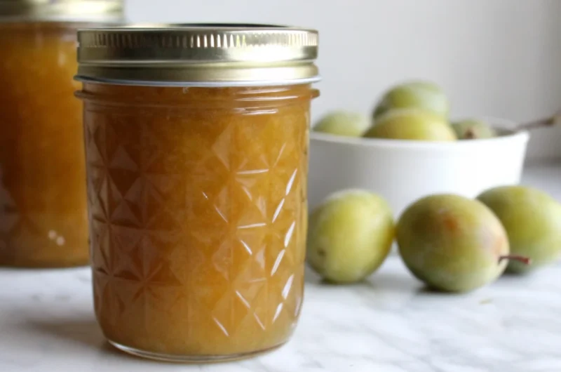 "Homemade greengage jam recipe in sterilized glass jars with fresh greengage plums and lemon on wooden cutting board