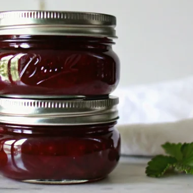 Homemade gooseberry jam in glass jars with fresh gooseberries scattered around on wooden table
