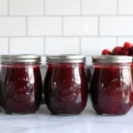 Homemade Christmas jam with cranberries and strawberries in glass jar with festive ribbon and cinnamon stick