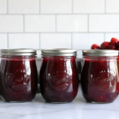 Homemade Christmas jam with cranberries and strawberries in glass jar with festive ribbon and cinnamon stick